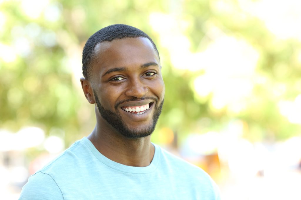 man is smiling at a camera in a park