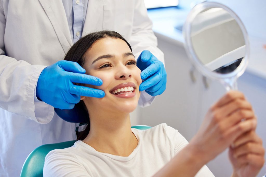 woman holding a handheld mirror to check her smile in a dental chair
